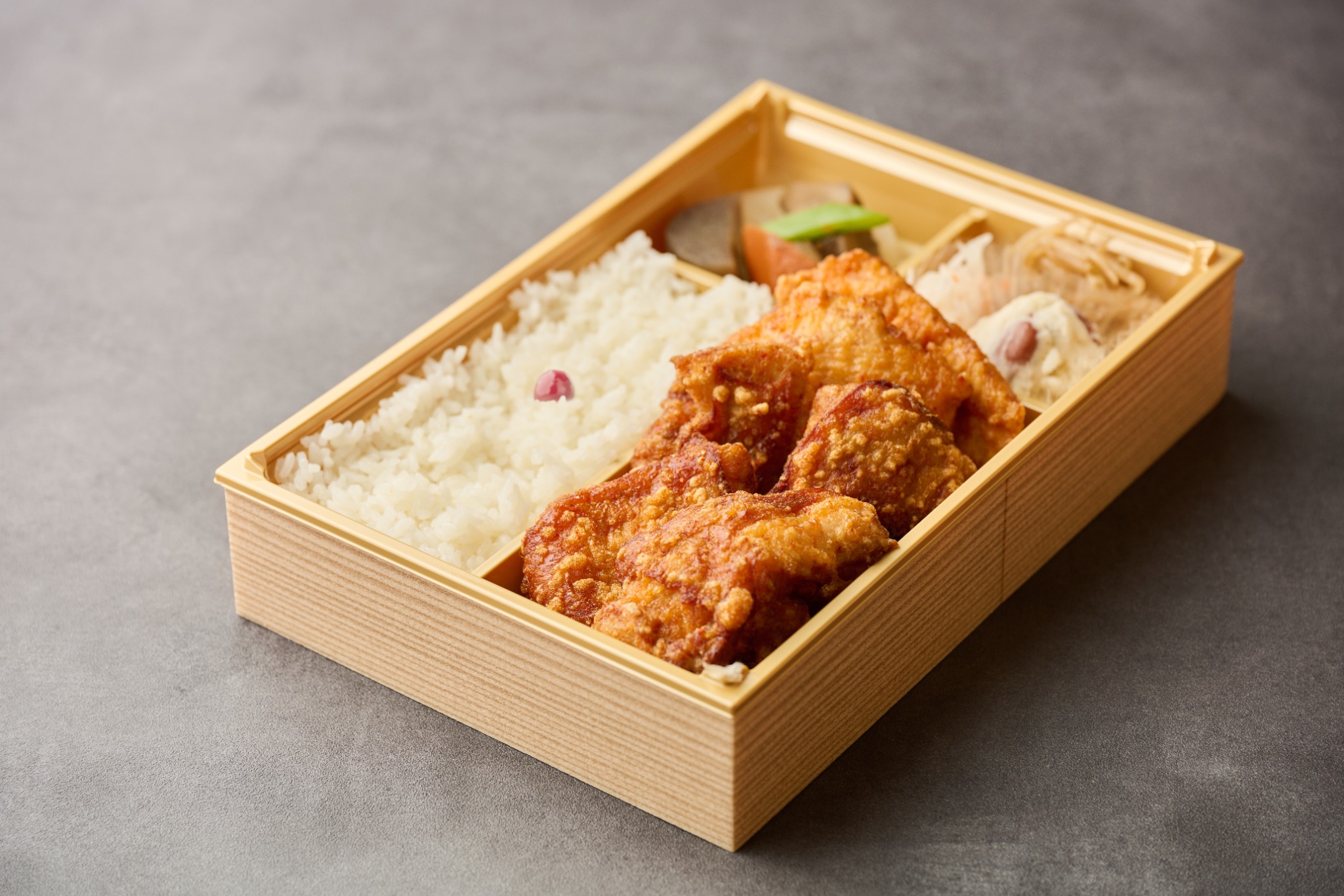 木目調の枠付き弁当箱に盛り付けた斉唐のから揚げ、ごはんと副菜